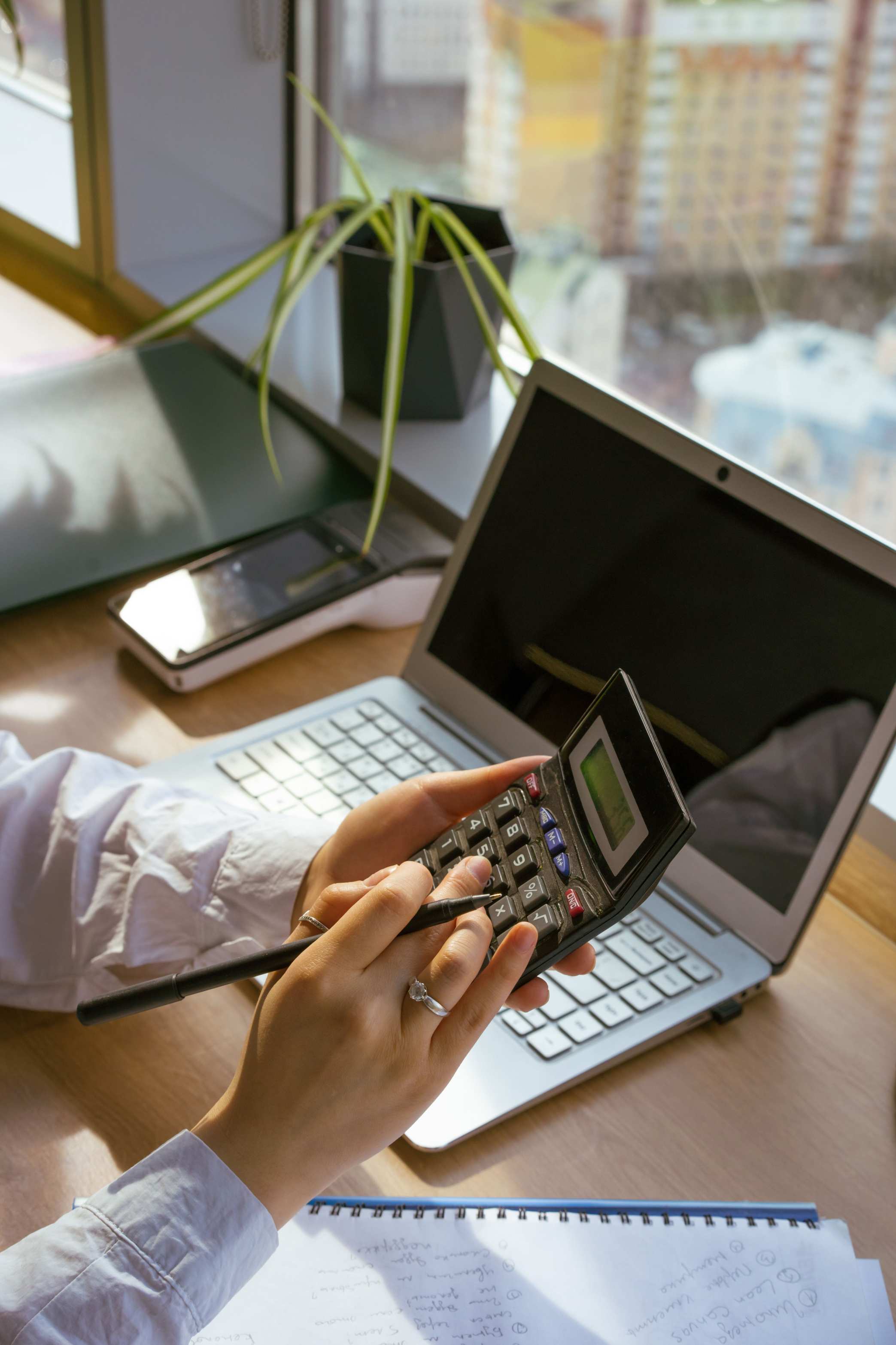 Hände an der Tastatur vor einem Bildschirm mit Zahlen — Person mit Laptop und Notizblock bei Finanzaufgaben
